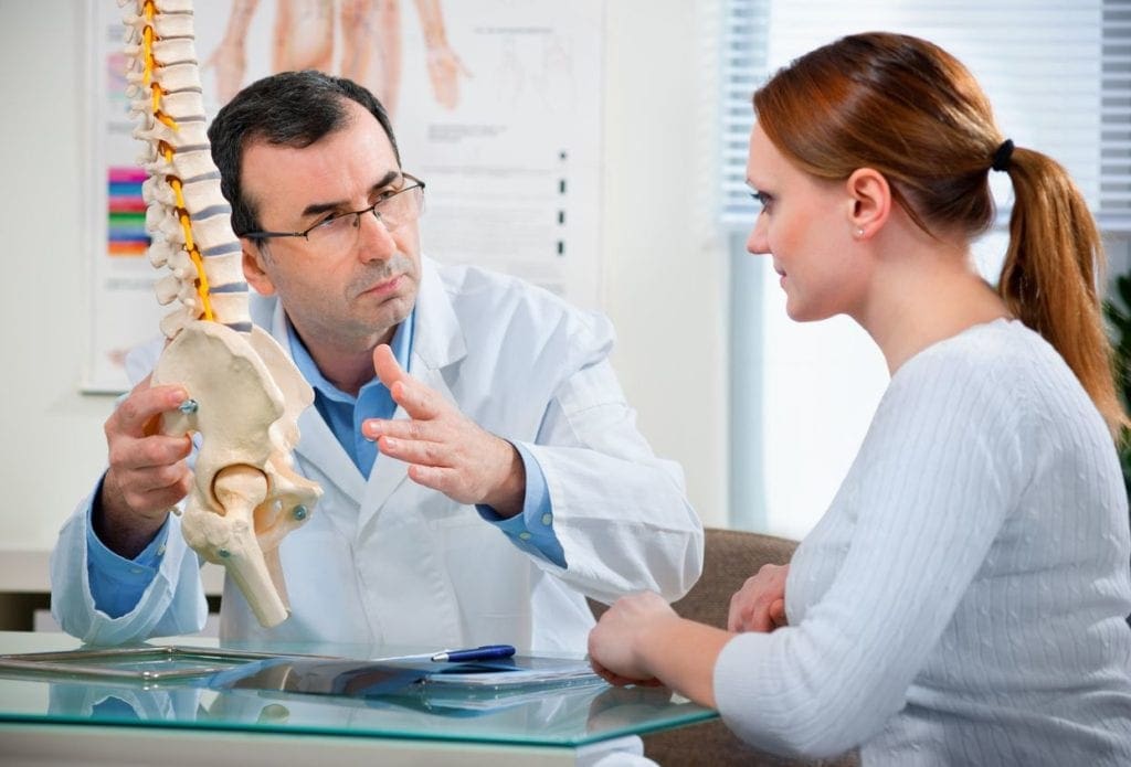 A doctor talking to a woman in front of a skeleton.