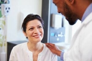 A woman smiling at the camera while being examined by a doctor.