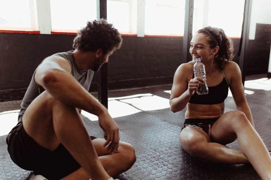 A man and woman sitting on the ground drinking water.