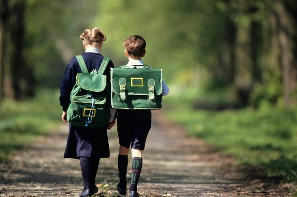 Two children are walking down a path with backpacks.