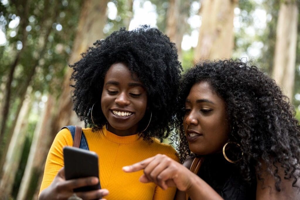 Two women looking at a cell phone in the woods.