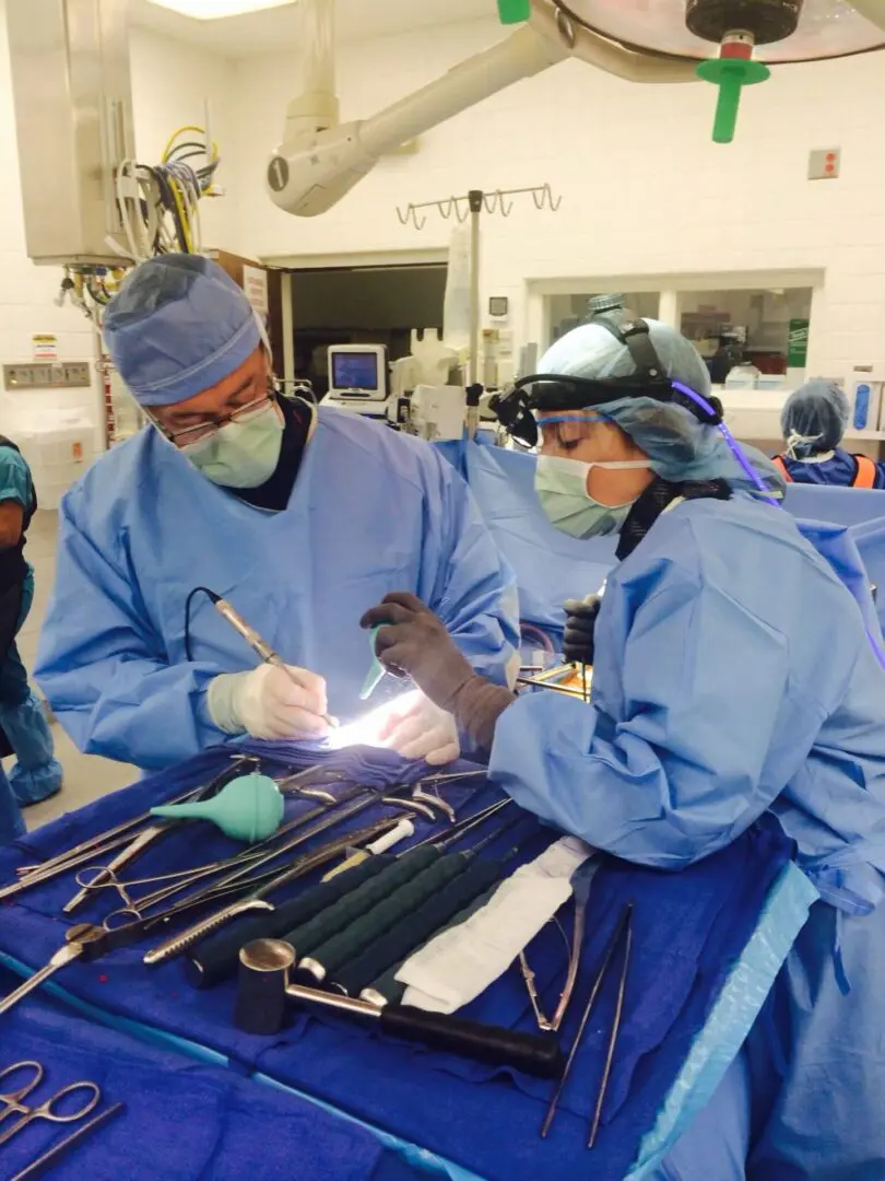 Two surgeons in blue gowns working on a patient.